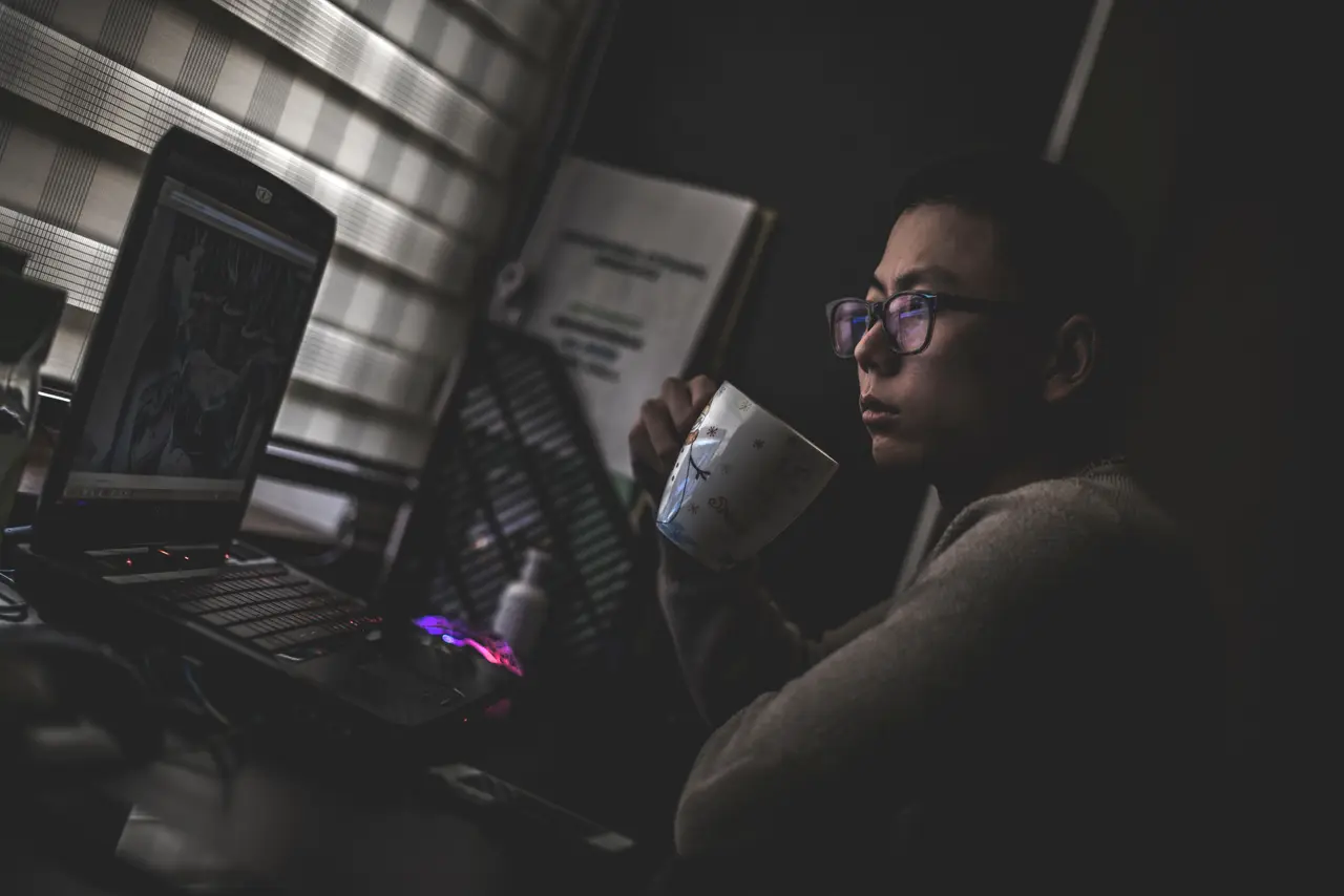 A person working at a laptop in a dark room lit by the screen