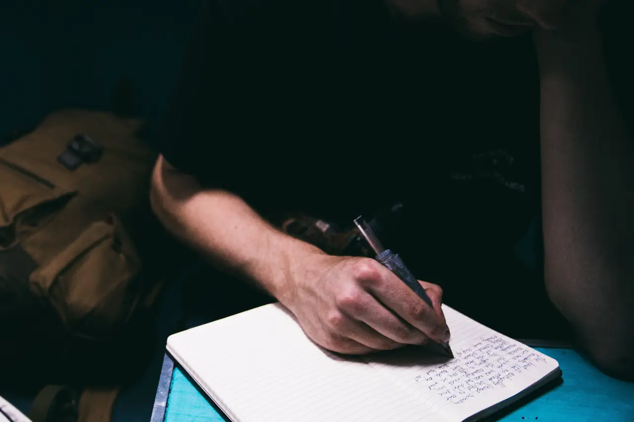 A hand writing in a notebook in low light