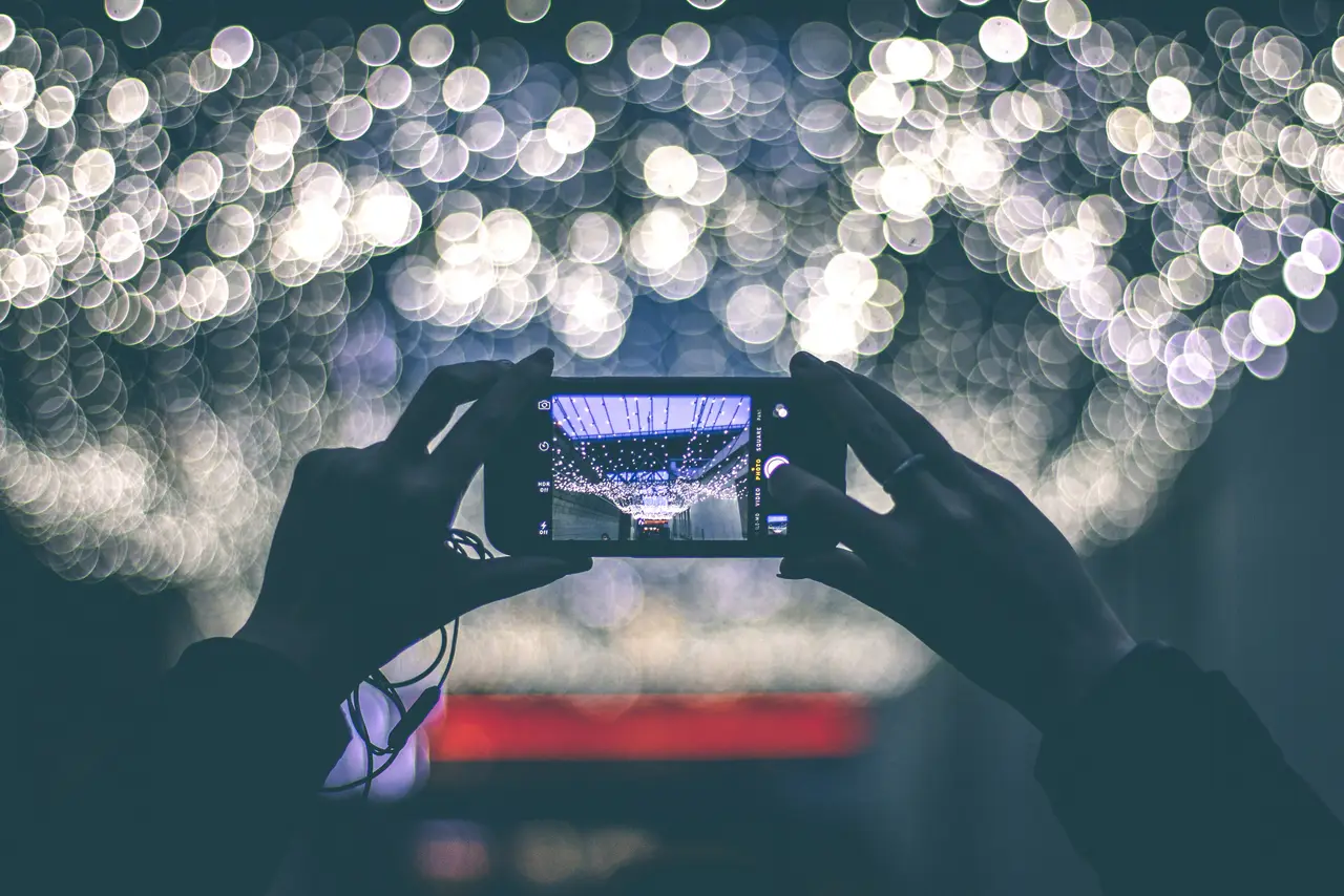 Hands holding a phone camera up to city lights at night