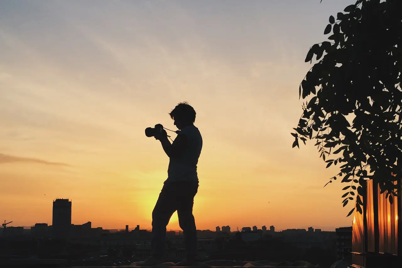Silhouette of a photographer framing a shot against a sunset skyline