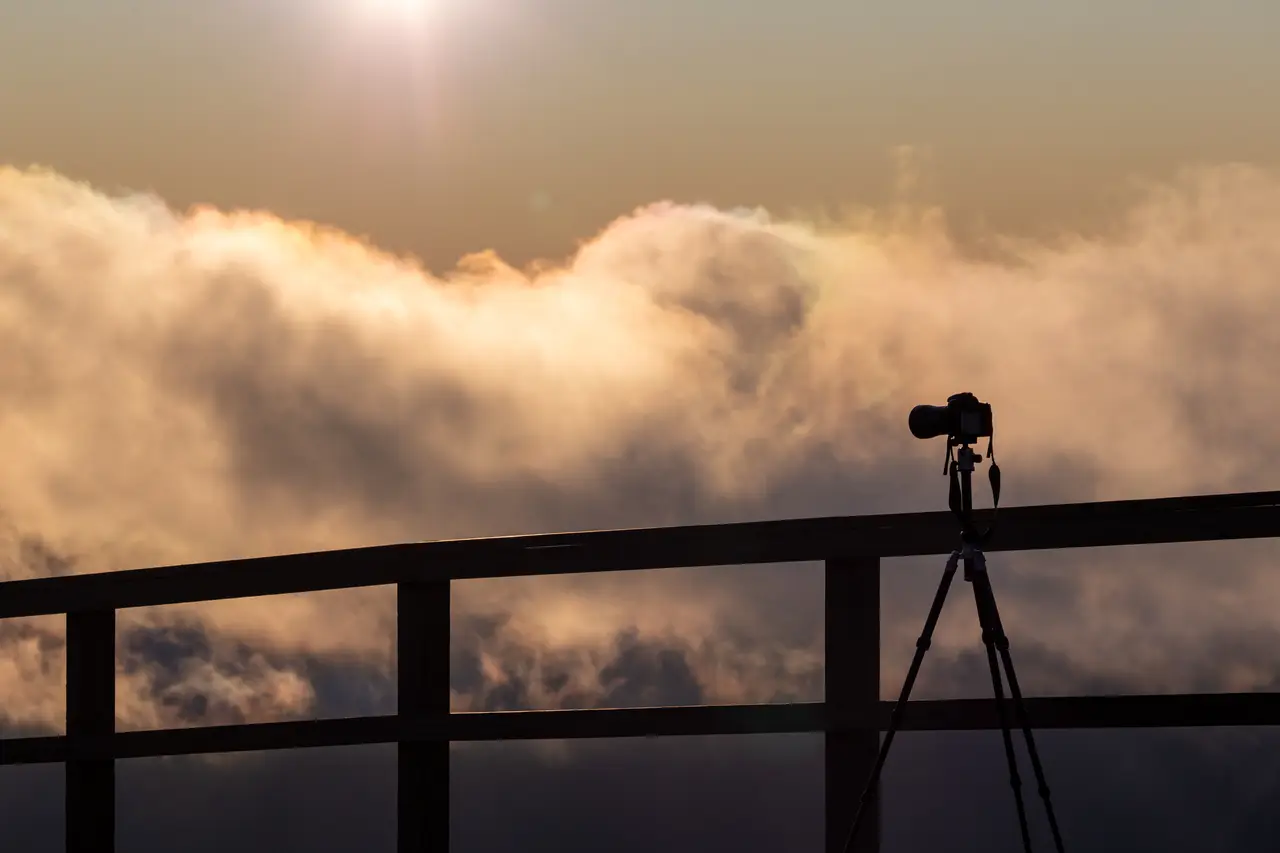 A camera on a tripod silhouetted above a sea of clouds